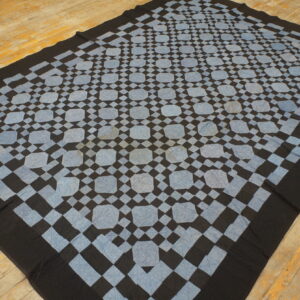 Black and pale blue geometric flat textile featuring octagonal shapes rests on distressed wood flooring.