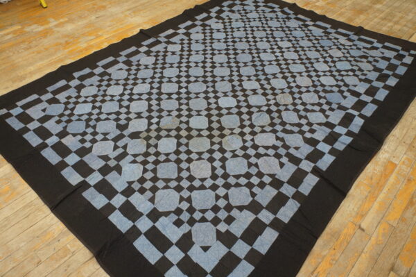 Black and pale blue geometric flat textile featuring octagonal shapes rests on distressed wood flooring.