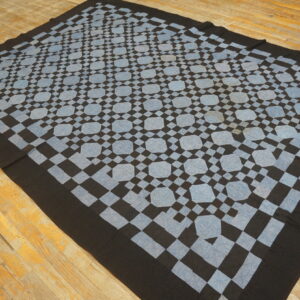 Black and pale blue geometric textile rug featuring repeating medallions rests on distressed wood flooring.