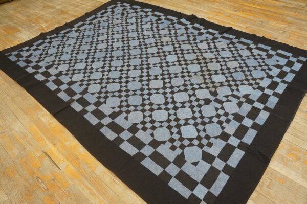 Black and pale blue geometric textile rug featuring repeating medallions rests on distressed wood flooring.