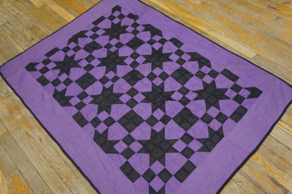 A purple and black geometric textile featuring stars rests on weathered yellow wood plank flooring.