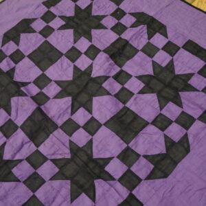 Geometric purple and black textile with a repeating star and diamond patchwork pattern on wood planks.