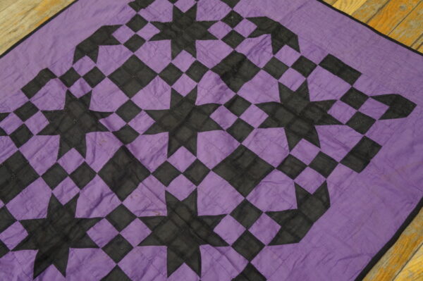 Geometric purple and black textile with a repeating star and diamond patchwork pattern on wood planks.