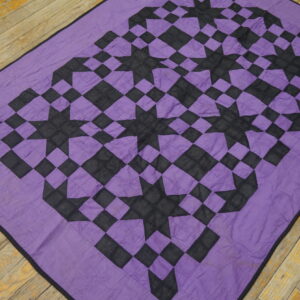 Purple and black geometric rug with repeating eight-pointed star motifs rests on rustic wooden floorboards.