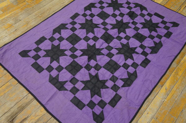 Purple and black geometric rug with repeating eight-pointed star motifs rests on rustic wooden floorboards.
