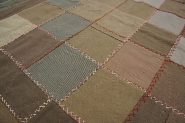 Muted brown, olive, and gray patchwork rug with varied textures and contrasting pink and red stitching.