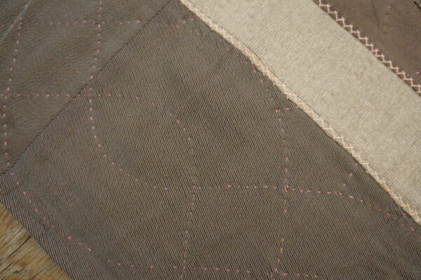 Dark ribbed patches with faint pink dotted patterns are joined by criss-cross stitching to light beige fabric.