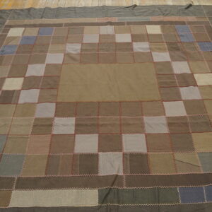 Patchwork rug features a grid of earth-toned squares with dark borders, visible on rustic wood plank flooring.
