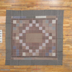 Muted gray and taupe patchwork rug with red stitched seams lies flat on distressed hardwood flooring.