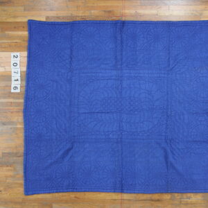 Blue quilted textile with detailed stitched medallions and curved patterns on a wooden floor.