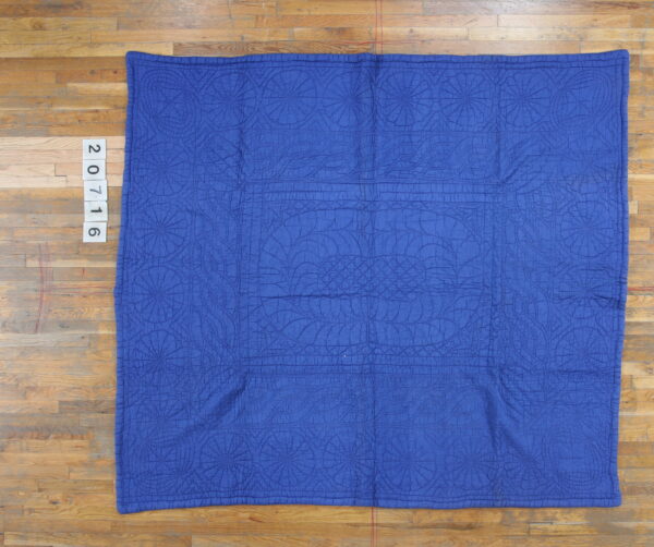 Blue quilted textile with detailed stitched medallions and curved patterns on a wooden floor.