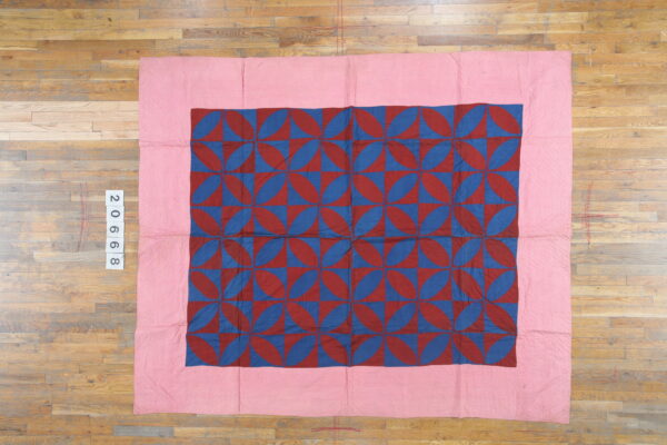A flat textile featuring a central geometric pattern of red and blue petal shapes with a wide pink border.