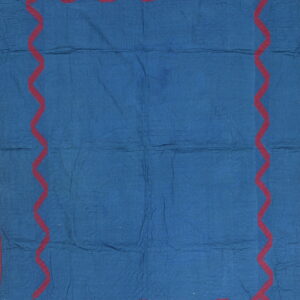 A blue quilted textile featuring a prominent dark red zigzag border design.