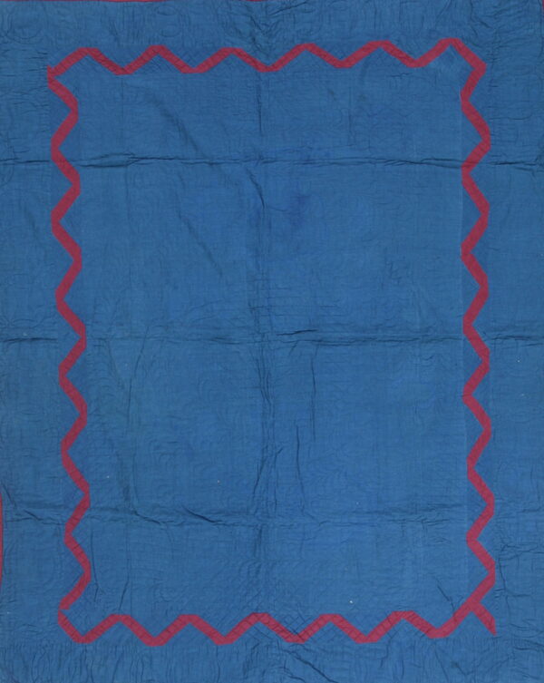 A blue quilted textile featuring a prominent dark red zigzag border design.