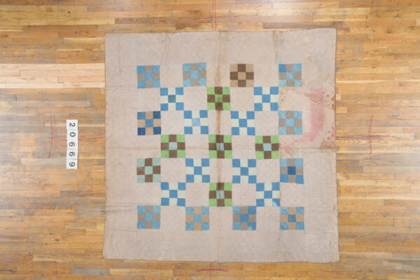 Low-pile beige textile with a geometric blue, green, and brown patchwork design rests on hardwood flooring.