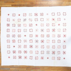 White flat textile with repeating pink and mauve star patterns lies on a hardwood floor beside a shoe.