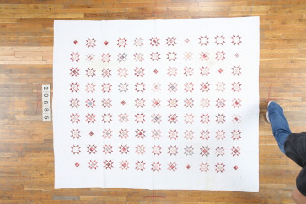 White flat textile with repeating pink and mauve star patterns lies on a hardwood floor beside a shoe.