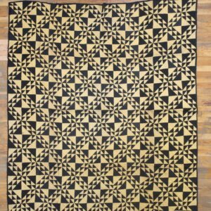A low-pile black and gold geometric rug with a dense triangular mosaic pattern rests on wood flooring.