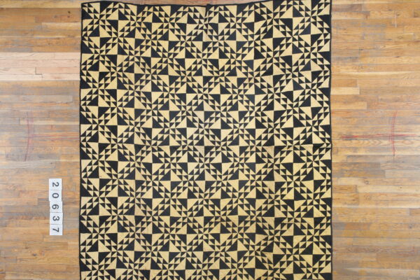A low-pile black and gold geometric rug with a dense triangular mosaic pattern rests on wood flooring.