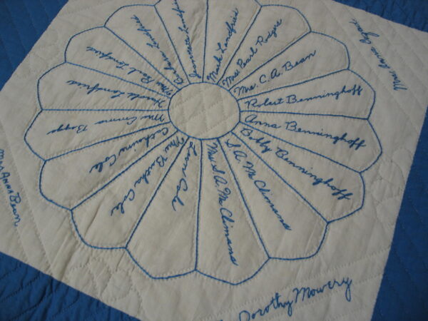 Low-pile cream textile featuring blue embroidered names within a circular petal design and quilted diamonds.