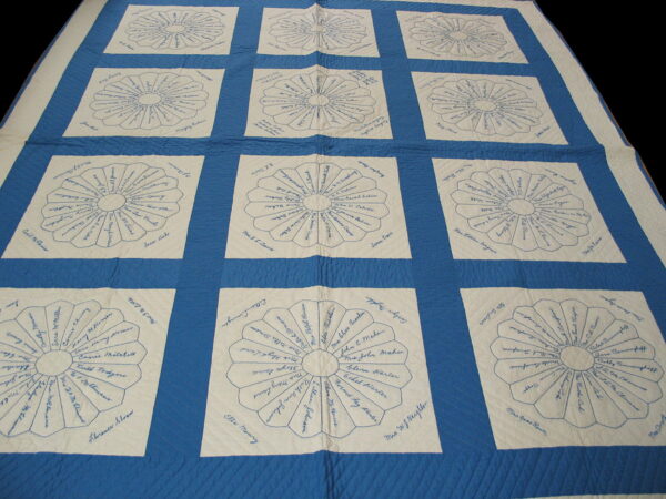 White squares featuring blue hand-drawn floral patterns and signatures are set within a grid of quilted blue fabric.
