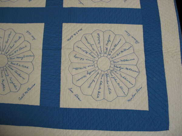 Close-up of a blue and white quilted textile with embroidered names in fan-shaped blocks.