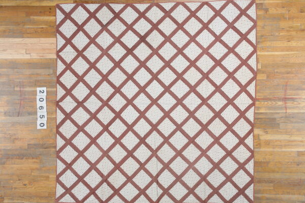 Cream rug with a reddish-brown lattice pattern and small interior dots on a light wood plank floor.