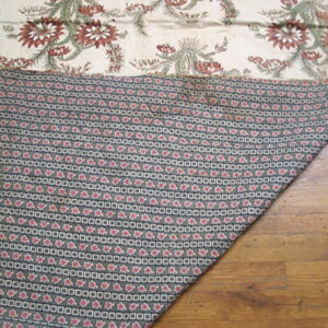 Cream botanical textile folded to show gray and red geometric backing resting on distressed wood flooring.