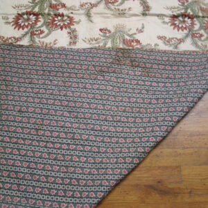 Cream, rust, and green floral textile face folded to show a dark geometric pattern on wood planks.