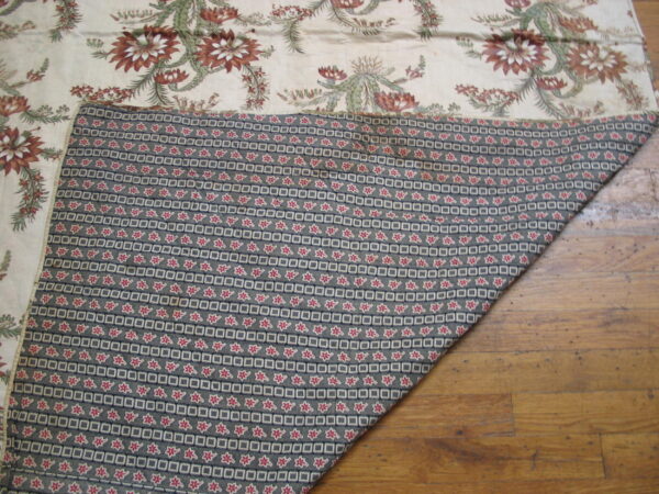 Cream, rust, and green floral textile face folded to show a dark geometric pattern on wood planks.