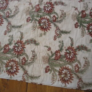 Flat beige rug with repeating rust and green floral and cactus motifs lies on wood flooring.