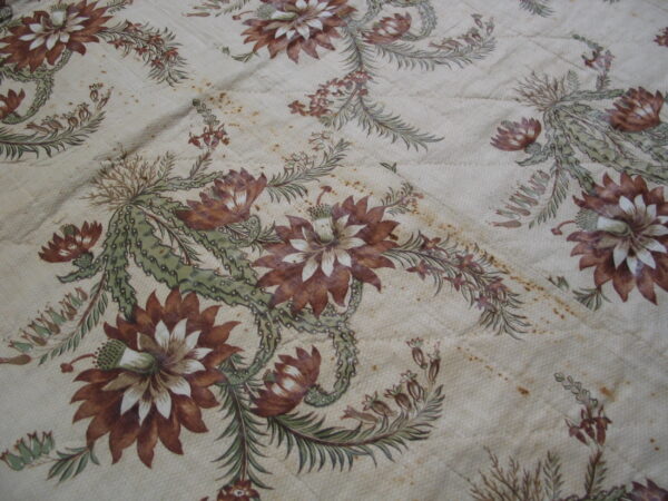 Beige low-pile textile with creases, featuring a repeating floral pattern of brown flowers and pale green vines.
