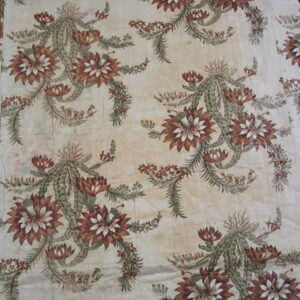 Flat-woven rug featuring repeating rust and green botanical motifs on a distressed cream background over wood flooring.