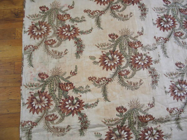 Flat-woven rug featuring repeating rust and green botanical motifs on a distressed cream background over wood flooring.