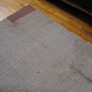 Blue-gray rug featuring diagonal stripes of red star motifs and white square patterns on hardwood.