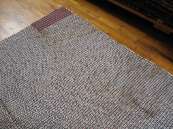 Blue-gray rug featuring diagonal stripes of red star motifs and white square patterns on hardwood.