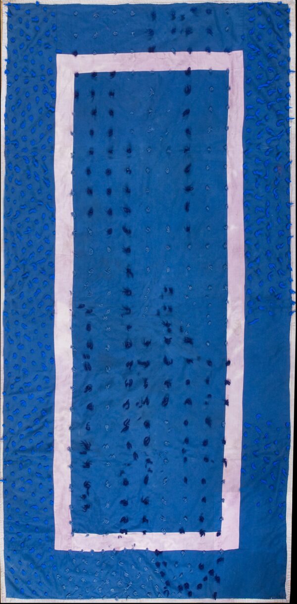 Blue low-pile rug with a pink inner border and varying blue textural knots rests on wood planks.