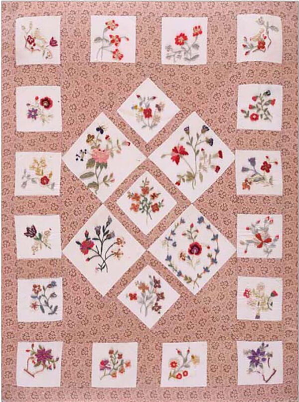 A rose-patterned textile features white square and diamond patches with colorful embroidered floral bouquets.