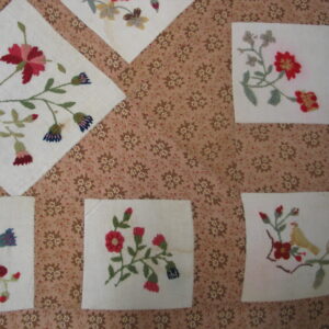 Needlepoint floral squares are stitched onto a patterned brown and beige textile background.