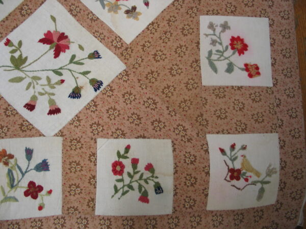 Needlepoint floral squares are stitched onto a patterned brown and beige textile background.