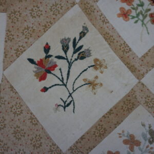 Close view of a high-pile needlework textile featuring multicolored floral diamonds bordered by printed beige strips.