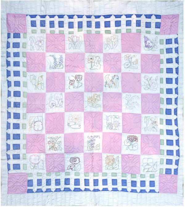 Quilted rug with pink and white checkerboard squares, featuring floral motifs and a blue and white fence border.