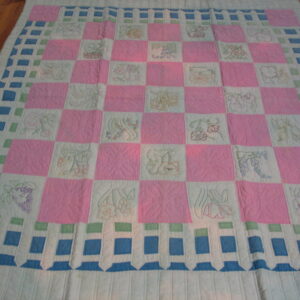 Quilted textile with a pink, white, and blue checkerboard pattern lying flat on dark wood flooring.