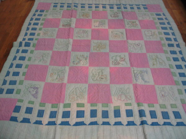 Quilted textile with a pink, white, and blue checkerboard pattern lying flat on dark wood flooring.