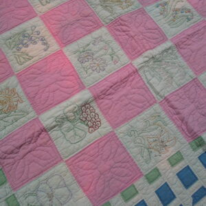 Close-up showing pink and pale green quilted squares with colorful embroidered floral motifs.