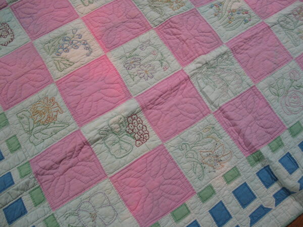 Close-up showing pink and pale green quilted squares with colorful embroidered floral motifs.