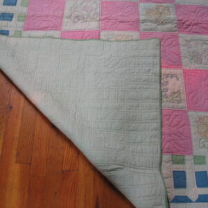 Quilted textile with pink and embroidered white floral blocks rests partially on vertical hardwood planks.