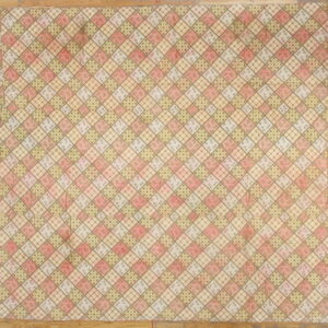 A muted textile featuring a diamond patchwork pattern in pink, olive, and brown rests on a hardwood floor.