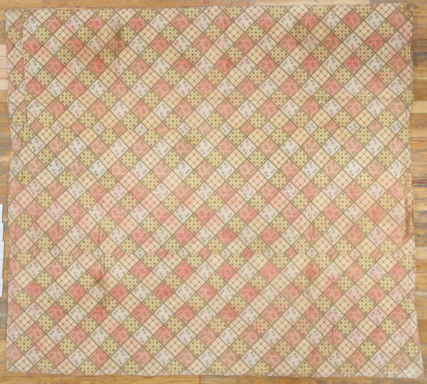 A muted textile featuring a diamond patchwork pattern in pink, olive, and brown rests on a hardwood floor.