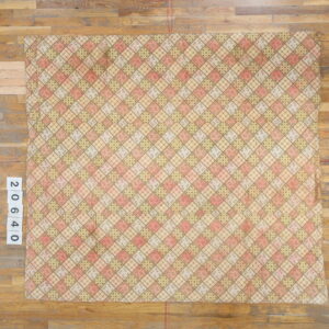 Pink, beige, and green argyle rug with assorted small patterns resting on a light wood floor.